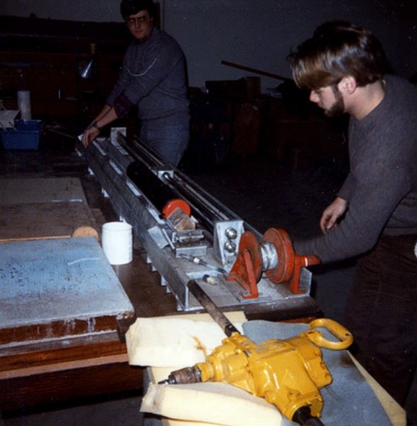 An unidentified technician uses the core-splitting machine to draw a knife blade through opposite sides of the plastic core liner at Woods Hole Oceanographic Institution (WHOI).
