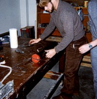 An unidentified technician slices the sediment lengthwise with a wire after the plastic core liner has been slit at the Woods Hole Oceanographic Institution (WHOI).