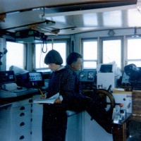 Captain "Dick" Colburn at the helm while Sally Needell maintains logs in the wheelhouse of the RV ASTERIAS.